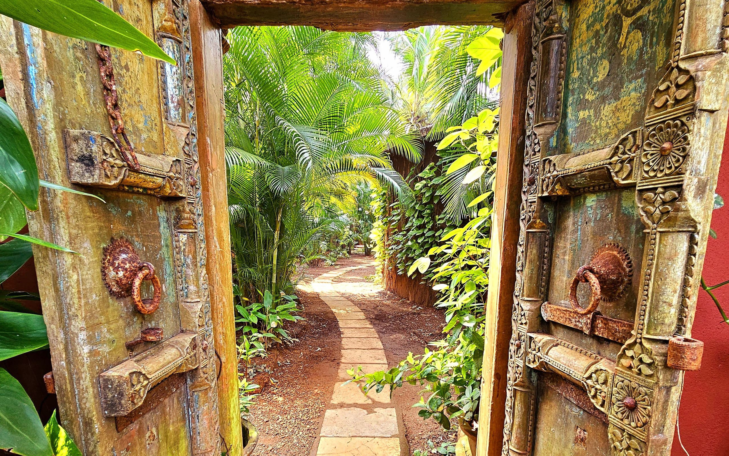 Carved doorway opening onto a garden path at Ashiyana, Goa